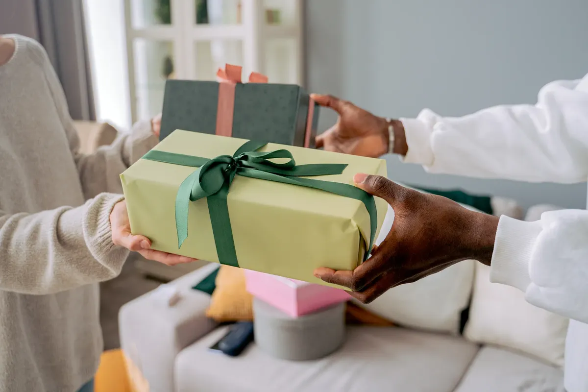Two people exchanging wrapped gifts indoors, highlighting a shared moment of giving.