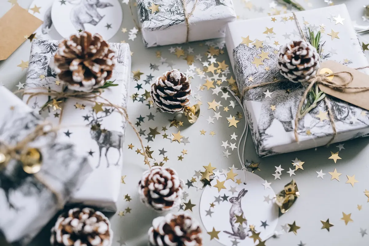 Overhead view of beautifully wrapped Christmas gifts with pine cones and star confetti.