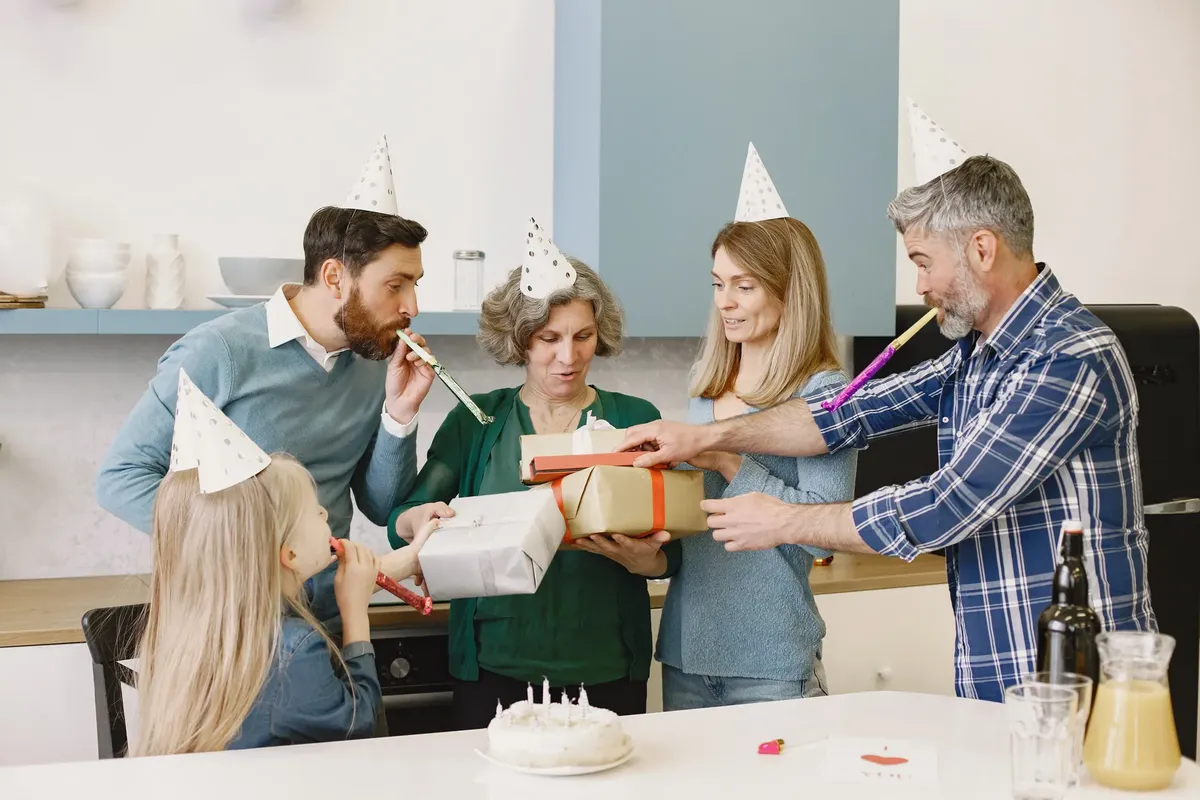 Happy family celebrating with party hats, gifts, and a cake indoors.